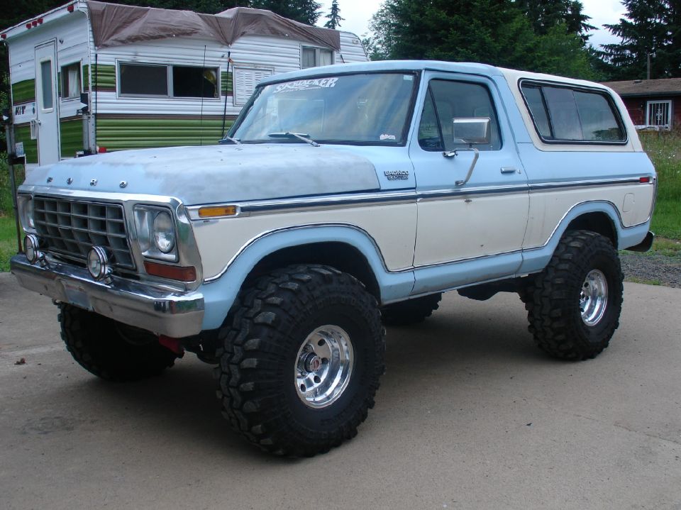 Lifted light blue and white 1978 Ford Bronco with big mud tires parked by vintage campers