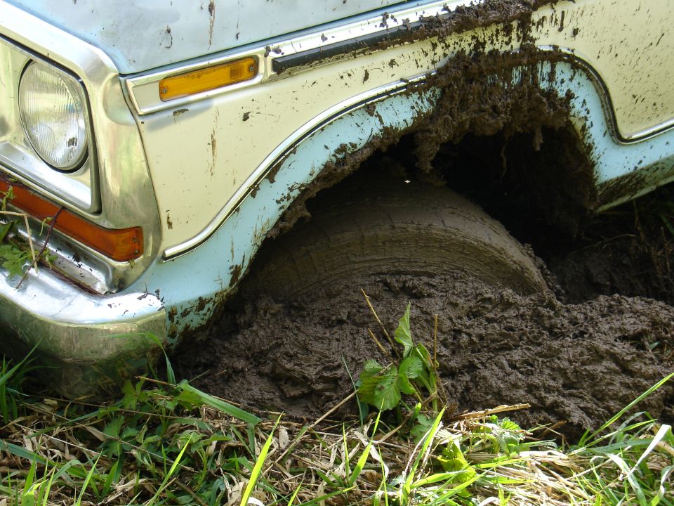 Front wheel of light blue vintage pickup truck stuck deep in mud