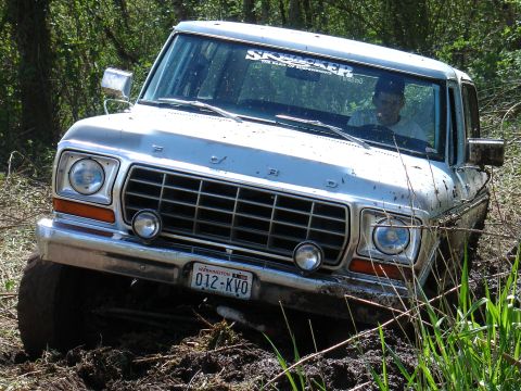 1978 Ford Bronco - This 1978 Ford Bronco is navigating a muddy trail, its front grille and headlights clearly visible.