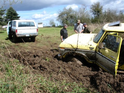 1978 Ford Bronco - Two trucks are stuck in a muddy field, with people gathered around the yellow truck.