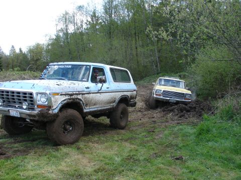 1978 Ford Bronco - Two off-road vehicles navigate a muddy trail through a wooded area.