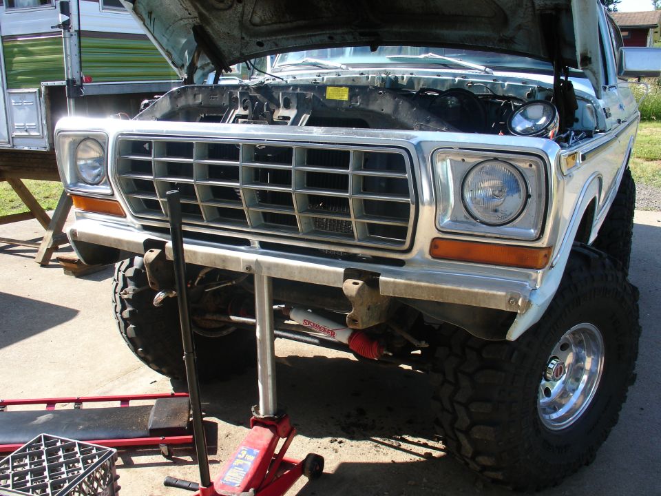 Lifted white 1970s Ford truck, hood up, chrome grille, Skyjacker stabilizer, mud tires