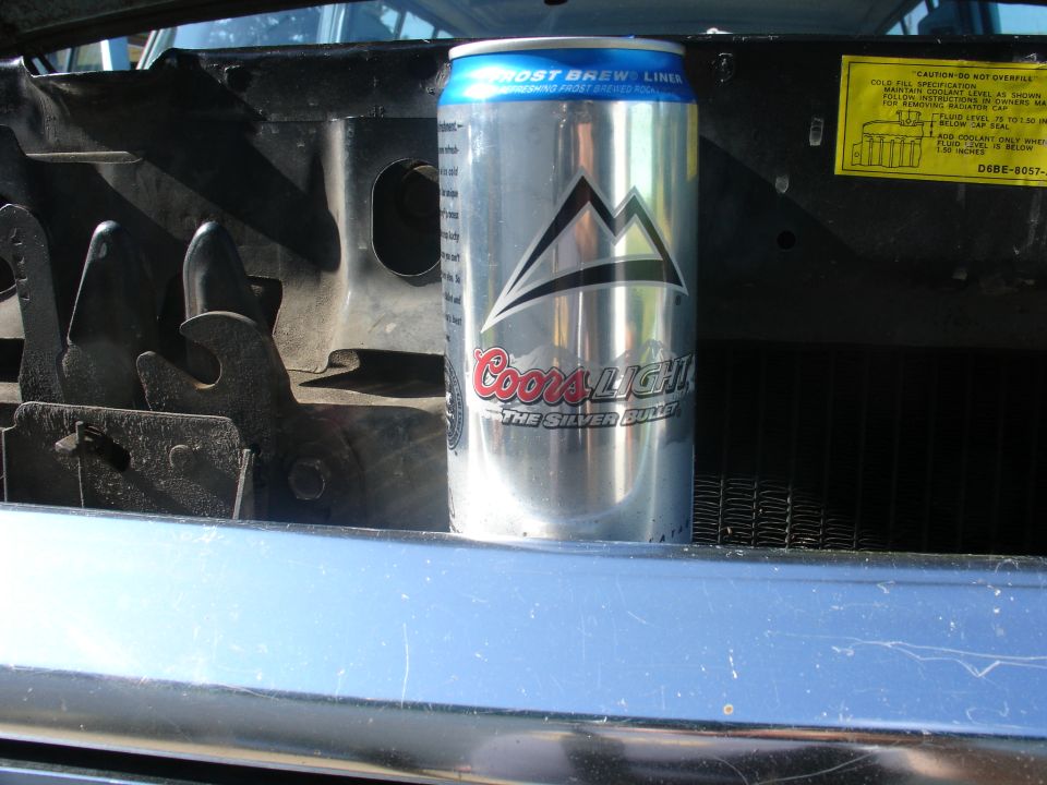 Coors Light can on radiator support beside yellow Ford coolant caution decal
