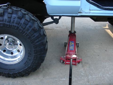 1978 Ford Bronco - Vehicle is being lifted by a hydraulic jack next to a large tire.