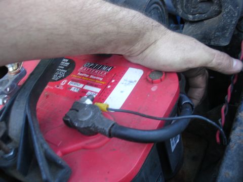 1978 Ford Bronco - Close-up of a red Optima battery with a hand reaching towards the wiring harness.