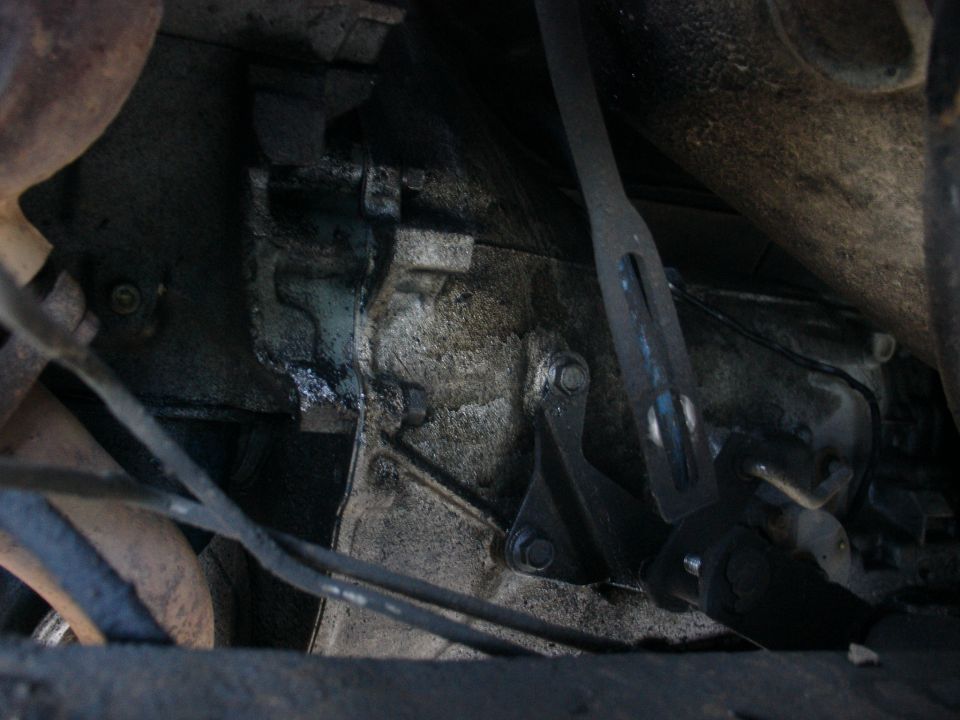 Grimy transmission housing with bolted steel shift linkage bracket seen from below