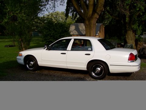 1999 Ford Crown Victoria - A white sedan is parked outdoors with trees in the background.