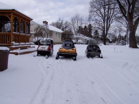 1999 Ford Crown Victoria - Three snowmobiles are parked in the snow next to a wooden gazebo.