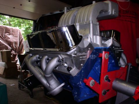 1993 Ford Bronco - Close-up of a supercharged V8 engine chrome valve covers and silver exhaust headers, with 'Edelbrock' branding visible.