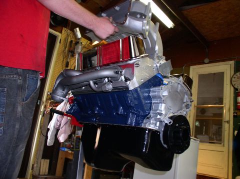 1993 Ford Bronco - A person is assembling a V8 engine, holding the intake manifold above the block.