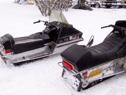 1999 Ford Crown Victoria - Two snowmobiles sit in a snowy outdoor setting, with a trailer visible in the background.