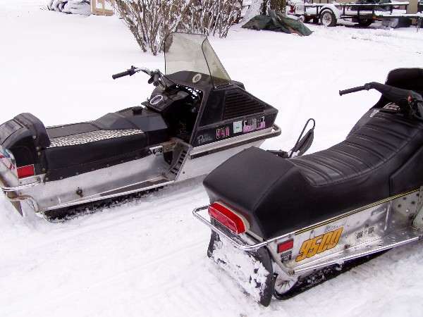 two snowmobiles parked in the snow, one black and silver, the other mostly black