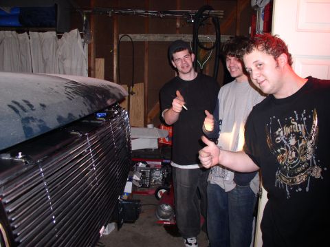 1993 Ford Bronco - Three friends pose in a garage next to the front of a vehicle with a large grille.