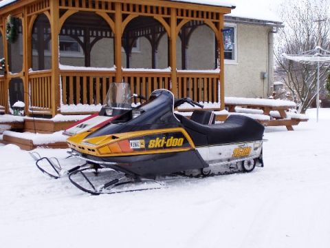1999 Ford Crown Victoria - A ski-doo snowmobile sits in the snow beside a wooden gazebo on a winter day.
