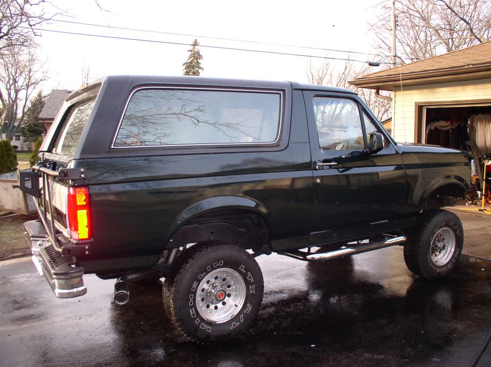 Dark green 1993 Ford Bronco parked on wet pavement, side view