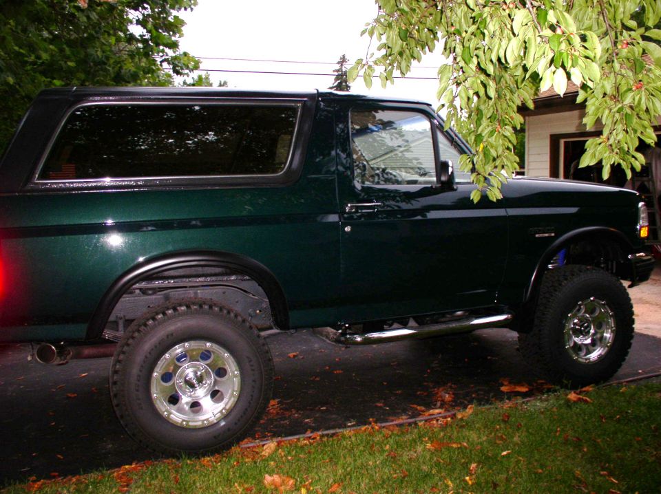 dark green Ford Bronco parked on asphalt, side view. Has aftermarket wheels and side steps