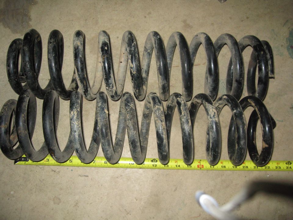 Two black coil suspension springs on concrete with a yellow tape measure