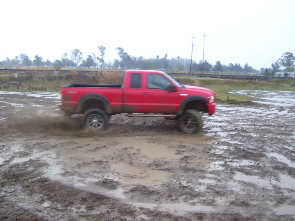 Red pickup truck driving through mud, kicking up spray