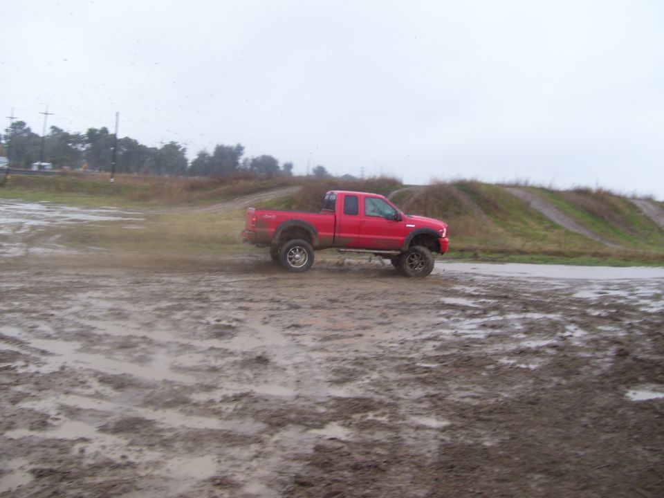 Red pickup truck driving through mud on an overcast day