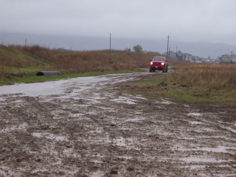 1986 Ford Bronco - A red pickup truck navigates a muddy, waterlogged road under a cloudy sky.