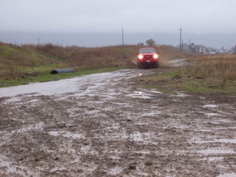 1986 Ford Bronco - A red truck navigates a challenging muddy terrain under an overcast sky.