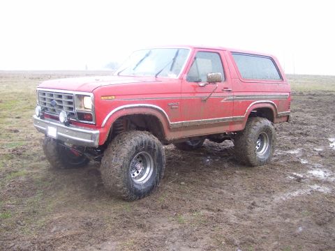 1986 Ford Bronco - This lifted Ford Bronco is shown off-road in a muddy field, highlighting its off-road capabilities.