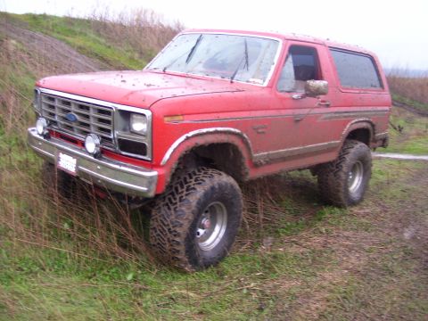 1986 Ford Bronco - Red 1986 Ford Bronco navigating a muddy off-road course.