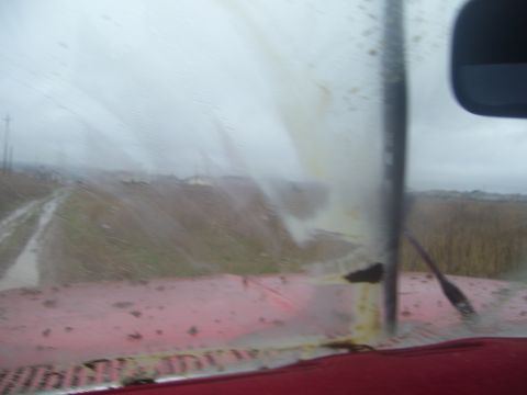 1986 Ford Bronco - The view from inside a vehicle shows a muddy road and fields through a dirty windshield on an overcast day.