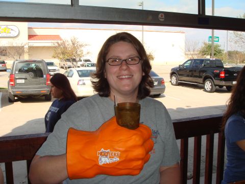 1992 Ford Bronco - A woman holds a large orange novelty glove while a black pickup truck and other vehicles are visible in the background.