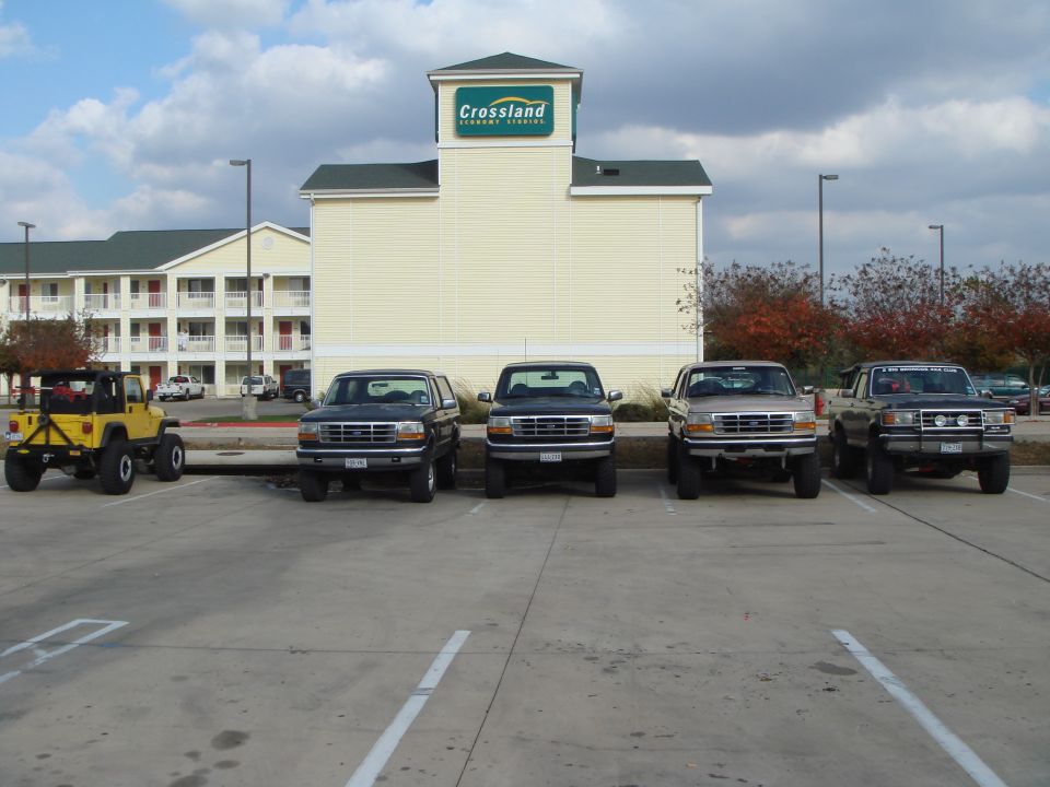 Four 1992 Ford Broncos parked in front of a hotel, one yellow Jeep Wrangler to the left