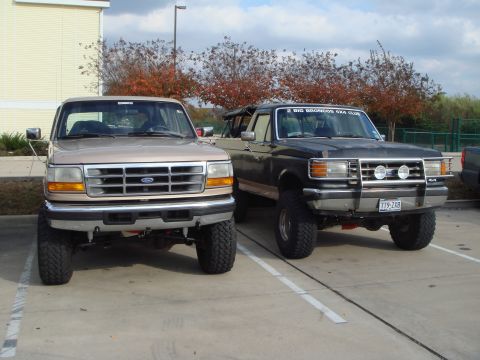 1992 Ford Bronco - Two Ford trucks, a tan one and a black one, are parked together outdoors.