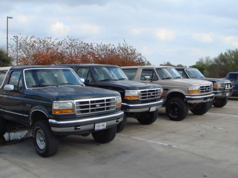 1992 Ford Bronco - A lineup of Ford Broncos and other SUVs are parked in a lot under a cloudy sky.