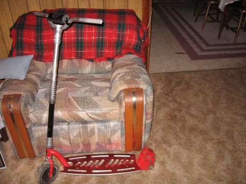 1992 Ford Crown Victoria - A red kick scooter is positioned in front of an armchair covered with a plaid blanket.