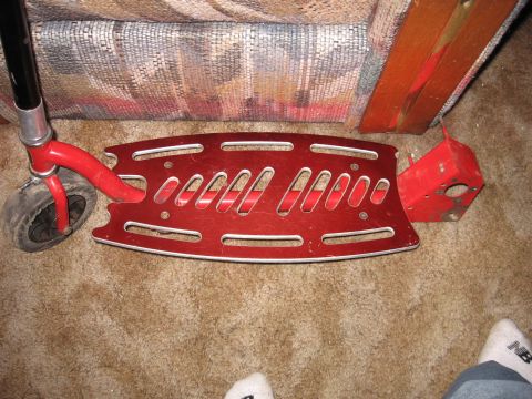 1992 Ford Crown Victoria - A red kick scooter's deck and front wheel are shown resting on a carpeted floor next to a chair.