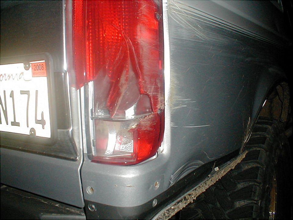 Damaged red taillight and scratched silver body panel on a vehicle with a 2008 California license plate