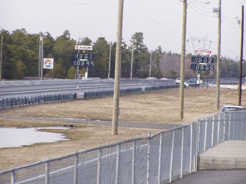1999 Ford Crown Victoria - A drag strip scene with scoreboards displaying times and a few vehicles visible in the distance.