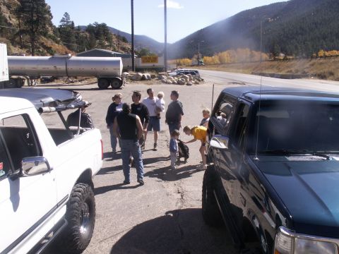 1986 Ford Bronco - A group of people stand around vehicles in a parking lot with mountains in the background.