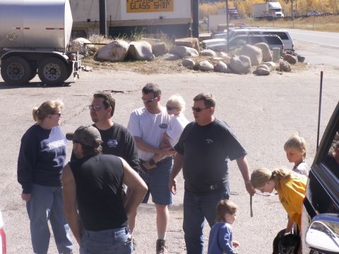 1986 Ford Bronco - A group of people are gathered in a parking lot with various vehicles and a large trailer visible.