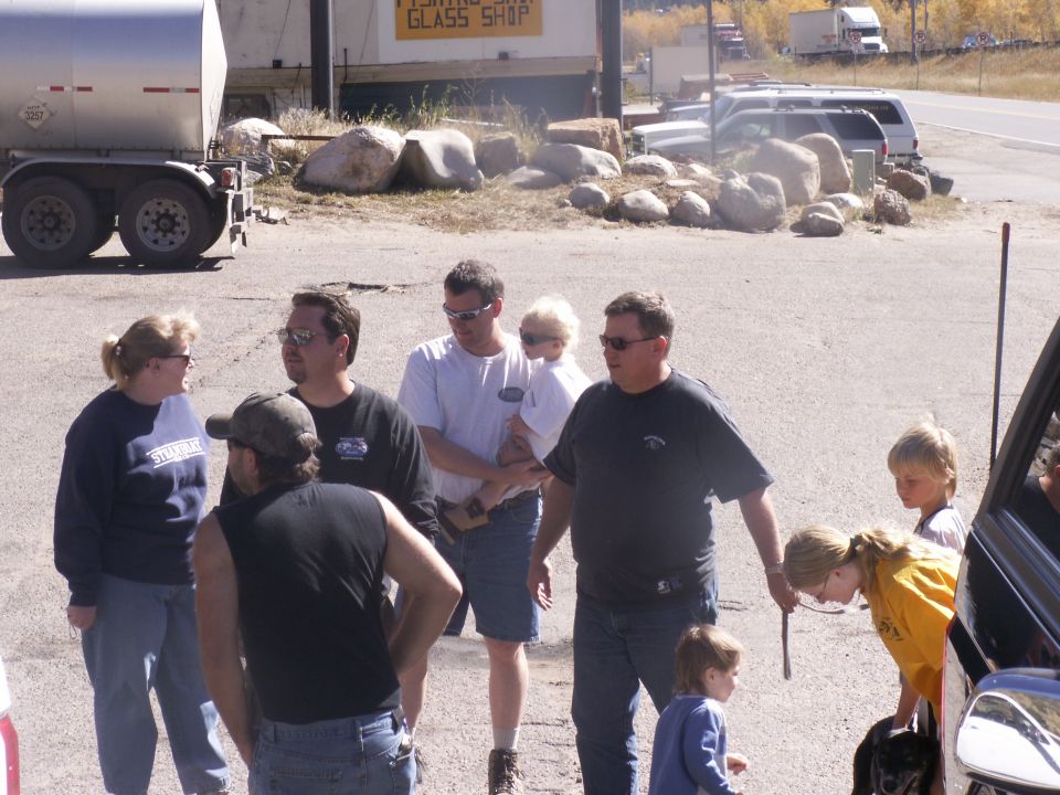 People stand in a parking lot near a large trailer and several vehicles, including SUVs and trucks