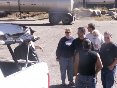 1986 Ford Bronco - A group of people stand around a damaged white pickup truck, with a large trailer visible behind them.