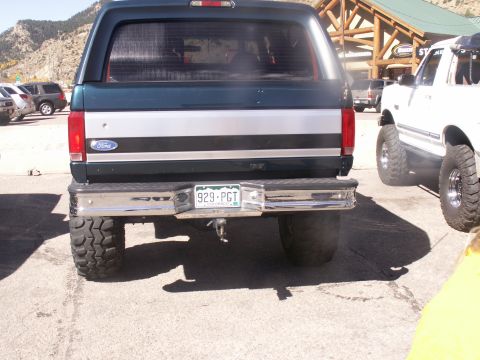 1986 Ford Bronco - Dark green Ford Bronco's rear is visible next to a white Bronco, with mountains in the background.