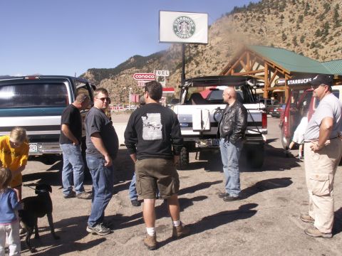 1986 Ford Bronco - Several people stand around a white Ford Bronco and a green truck in a parking lot with a Starbucks in the background.