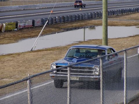 1999 Ford Crown Victoria - A blue 1965 Ford Fairlane sits on the side of a drag strip, with another vehicle in the background.