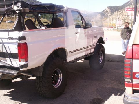 1986 Ford Bronco - A lifted white Ford Bronco is parked outdoors, with mountains in the background and another vehicle to its right.
