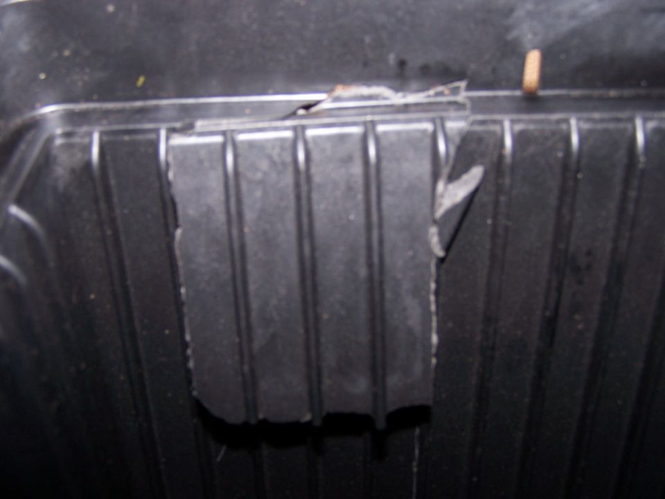 Close-up of a black plastic air filter housing with ribbed texture and torn insulation
