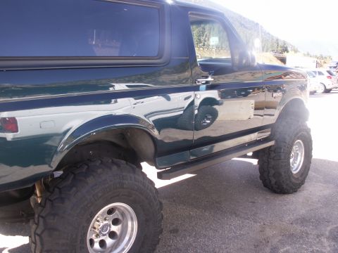 1986 Ford Bronco - This Ford Bronco features a lifted suspension and aftermarket wheels, with a reflection of another vehicle visible in its side panel.