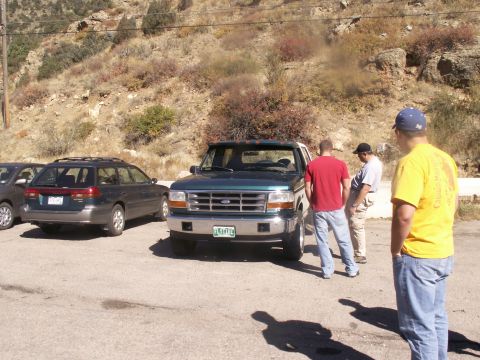 1986 Ford Bronco - A green Ford F-Series truck is parked in a lot with other vehicles and people nearby.