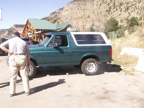 1986 Ford Bronco - Side view of a green Ford Bronco with a white top, parked outdoors.