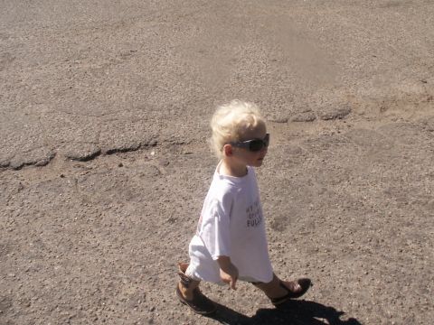 1986 Ford Bronco - A young child walks across a paved area, wearing sunglasses and cowboy boots.
