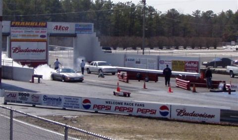 1999 Ford Crown Victoria - A drag racing event is underway with cars on the track and spectators in the background.